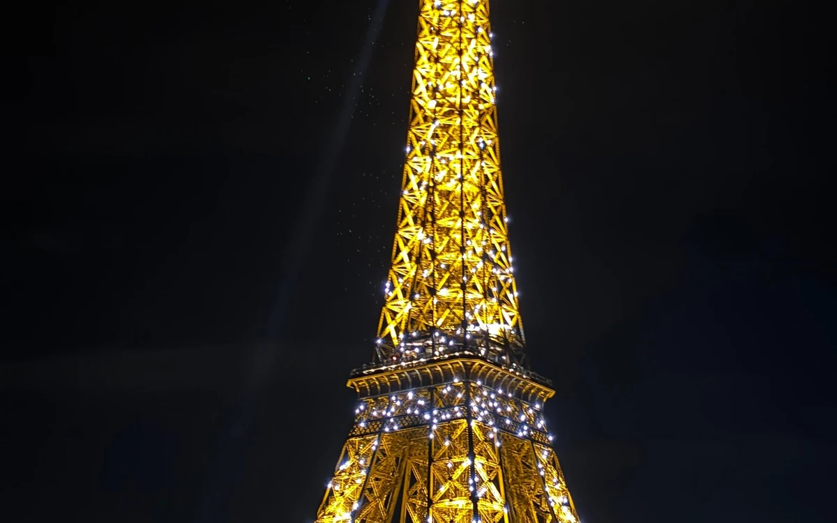 A glass-roofed dinner cruise boat on the Seine passing the illuminated Eiffel Tower in Paris